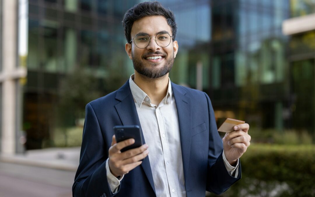Hispanic businessman holding smartphone and credit card outdoors in modern urban setting